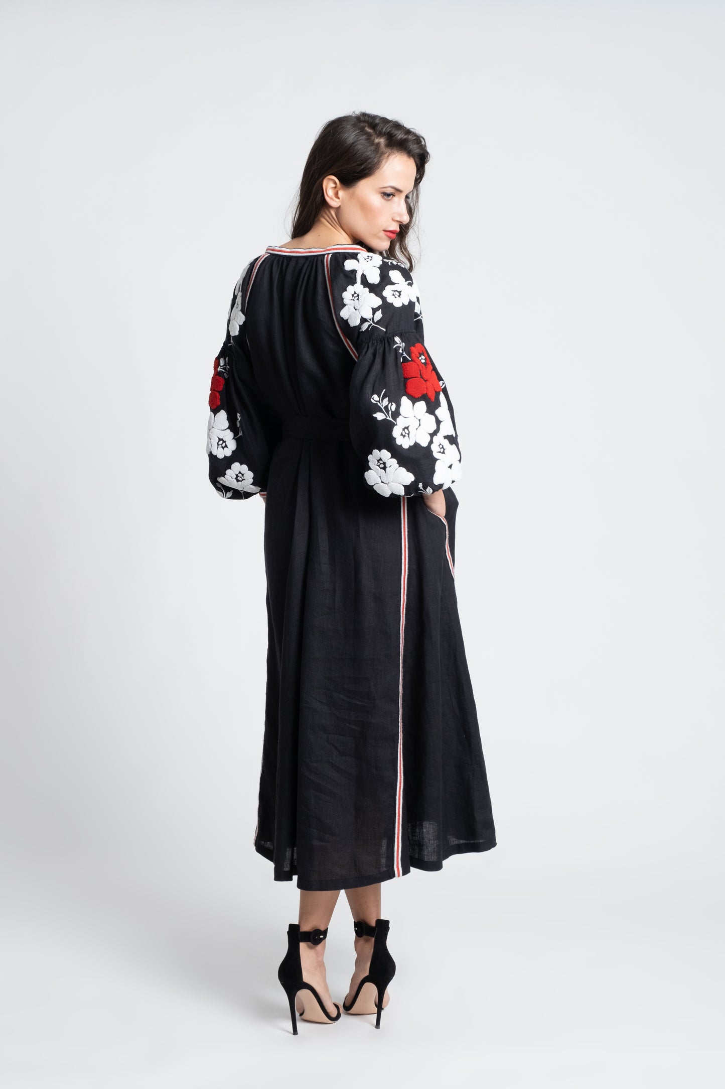 Malibu: Vestido de lino negro bordado en blanco y rojo, con cinturón, pompones y botones de nácar.